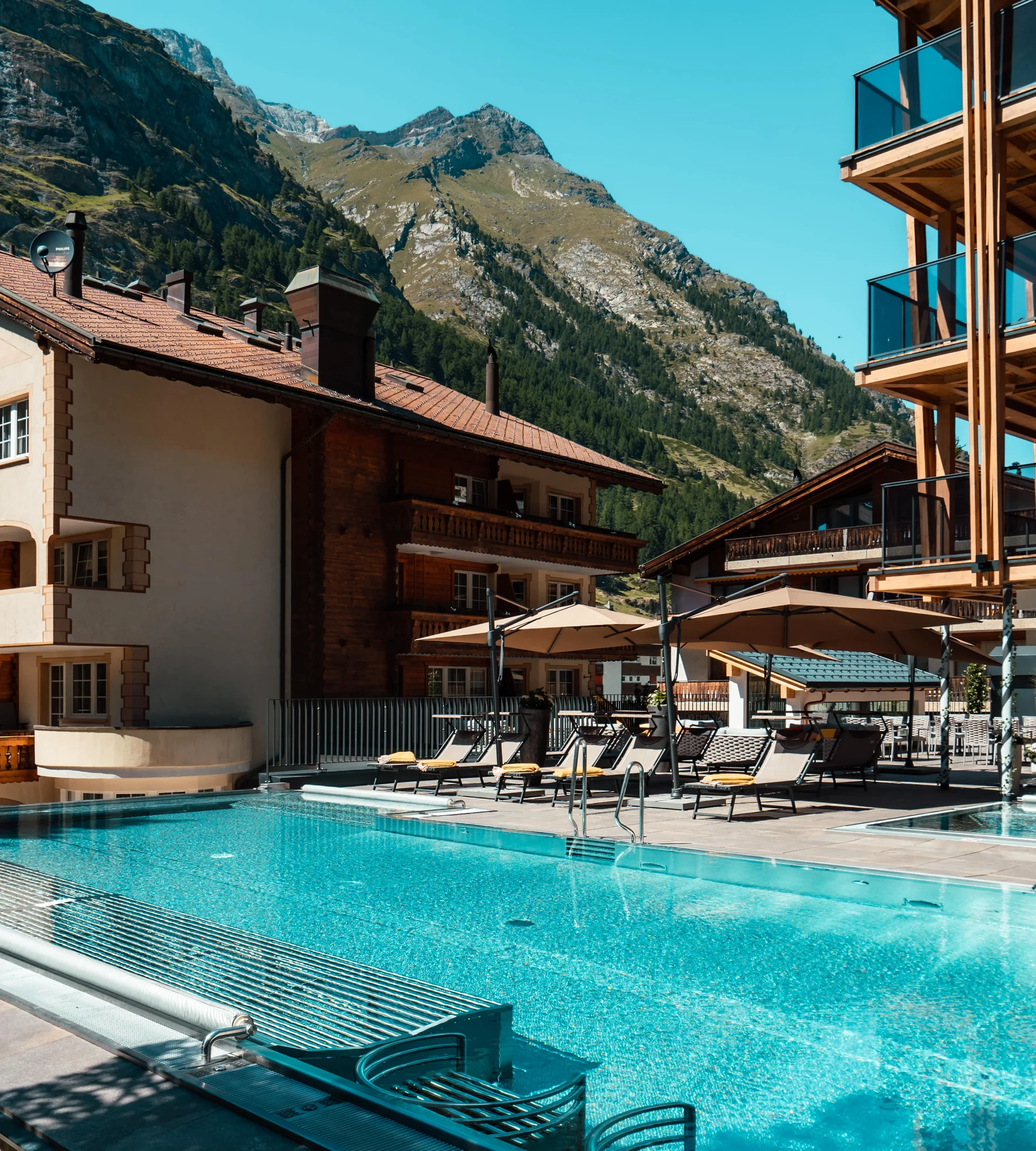 Ferien mit Kindern in Zermatt - Resort La Ginabelle Zermatt Infinitypool mit Terrasse und Bergen im Hintergrund im Sommer.