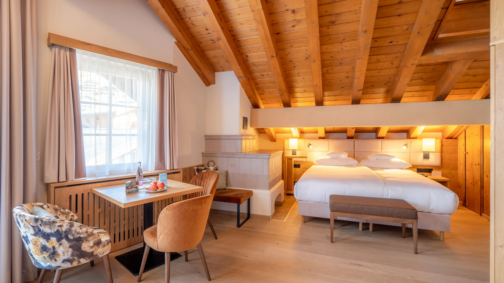Zimmer, Appartements & Suiten - Resort La Ginabelle Zermatt Gemütliches Hotelzimmer mit Holzdecke, Doppelbett und kleinem Tisch am Fenster