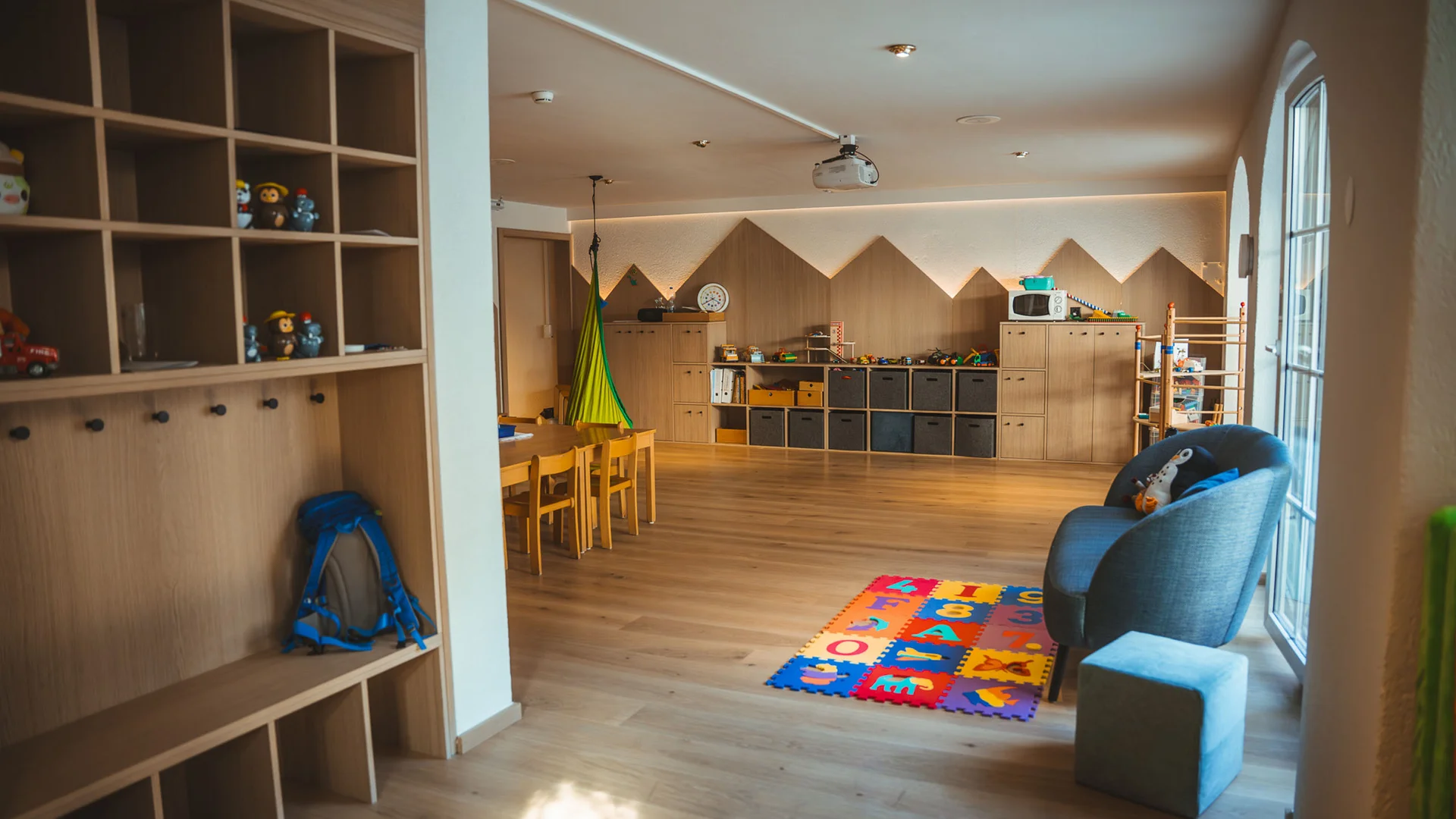 Ferien mit Kindern in Zermatt - Resort La Ginabelle Zermatt Kinderspielzimmer mit Holzregalen, Spielzeug und bunter Spielmatte