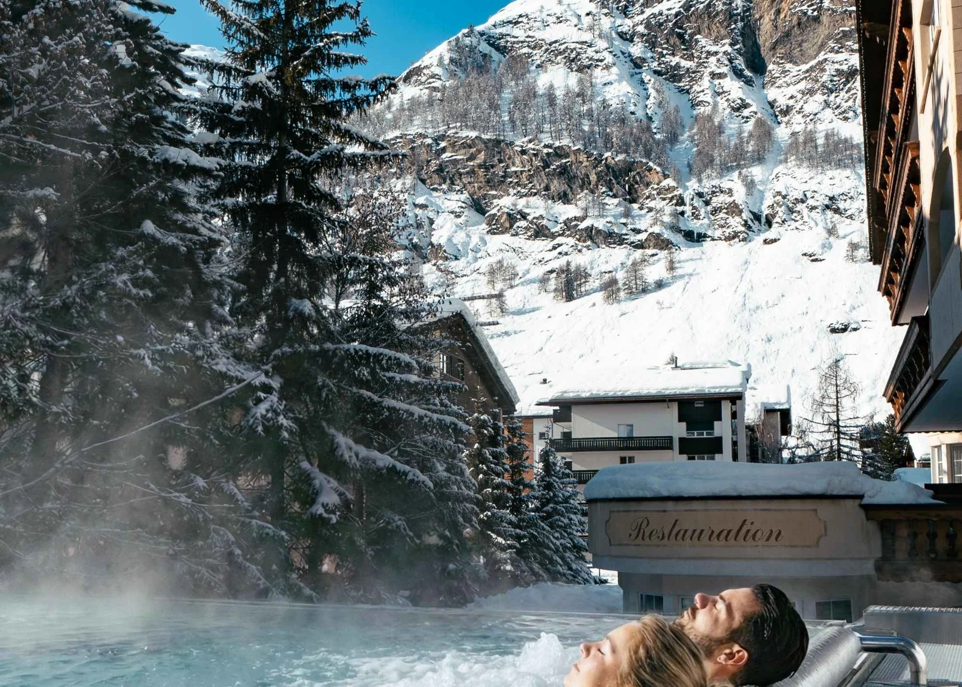 Wellnesshotel in Zermatt | GinaSPA im Resort La Ginabelle Menschen im Infinitypool mit Massagedüsen und Aussicht auf die verschneiten Berge im Winter.