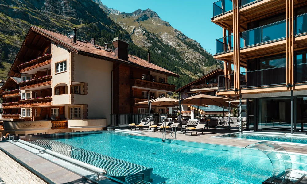 Wellnesshotel in Zermatt | GinaSPA im Resort La Ginabelle Infinitypool mit Terrasse und Bergen im Hintergrund im Sommer.