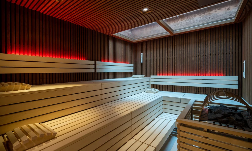 Wellnesshotel in Zermatt | GinaSPA im Resort La Ginabelle Finnische Sauna mit Holzbänken und indirekter roter Beleuchtung.