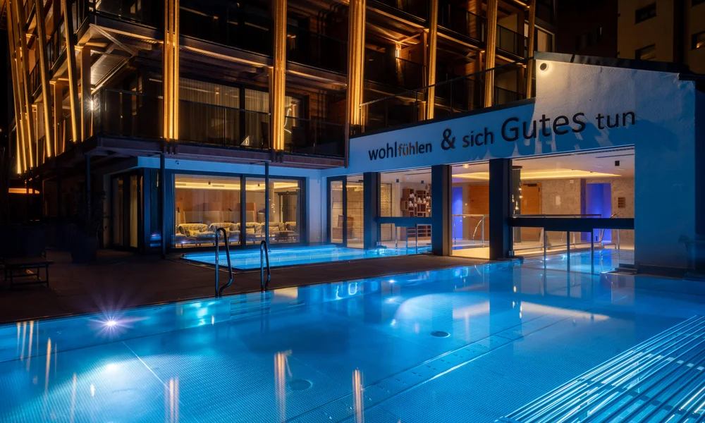 Wellnesshotel in Zermatt | GinaSPA im Resort La Ginabelle Beleuchteter Infinitypool mit beleuchtetem Hotel im Hintergrund in der Nacht.