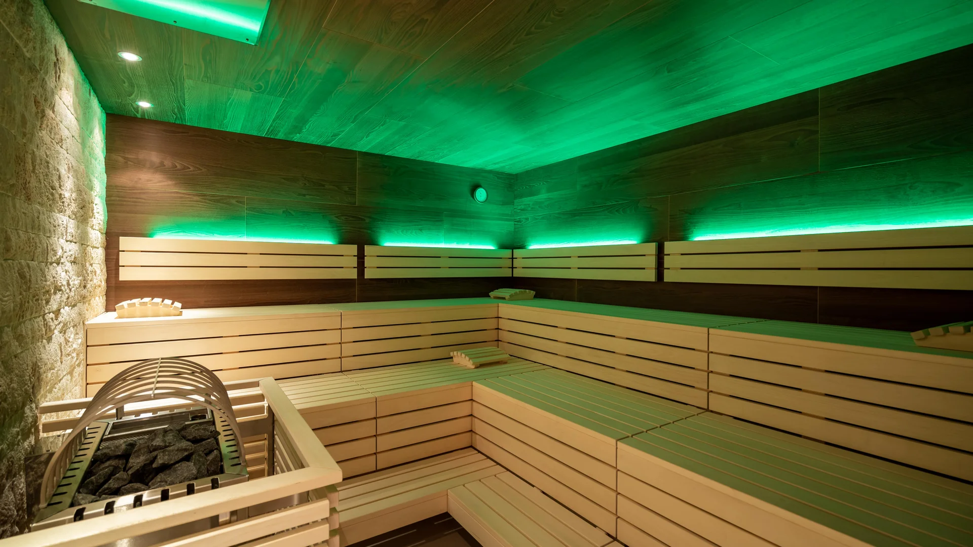 Wellnesshotel in Zermatt | GinaSPA im Resort La Ginabelle Bio Sauna mit indirekter grüner Beleuchtung, Holzbänken und in Holz verkleiderter Ofen.